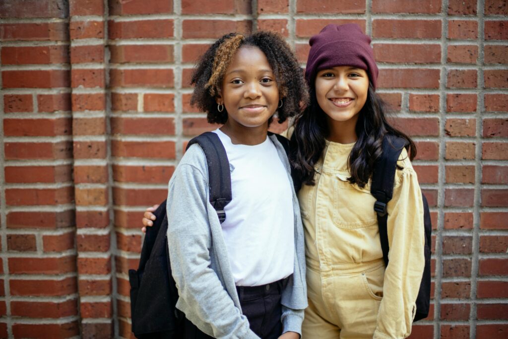 Happy diverse schoolgirls against brick wall